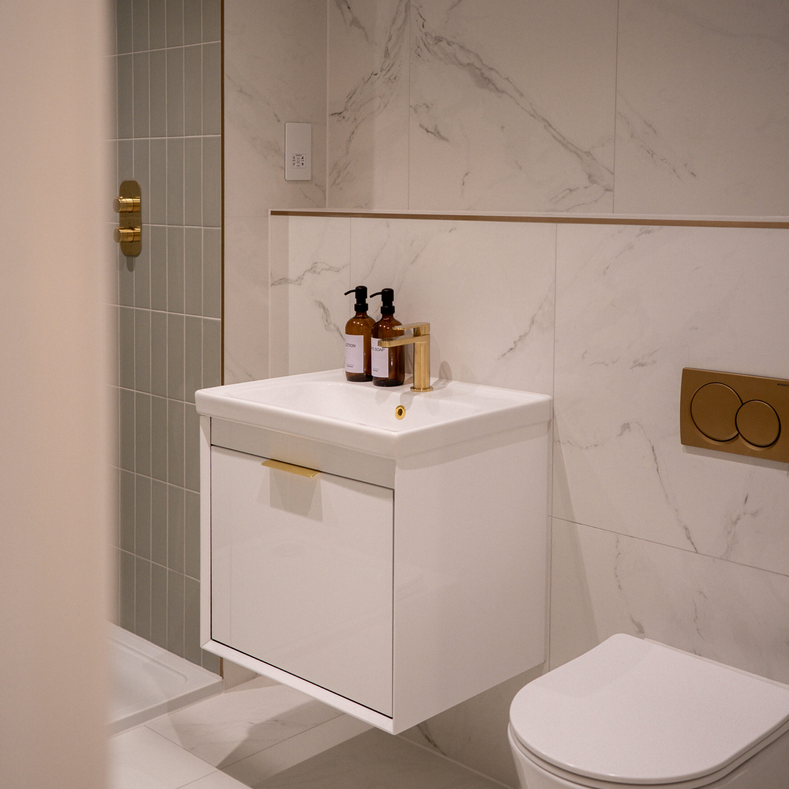 Shot of the ensuite in the main bedroom, marble tiling with gold feature finishes and sage green tiling within the shower. Floating white basin sink with gold finishes
