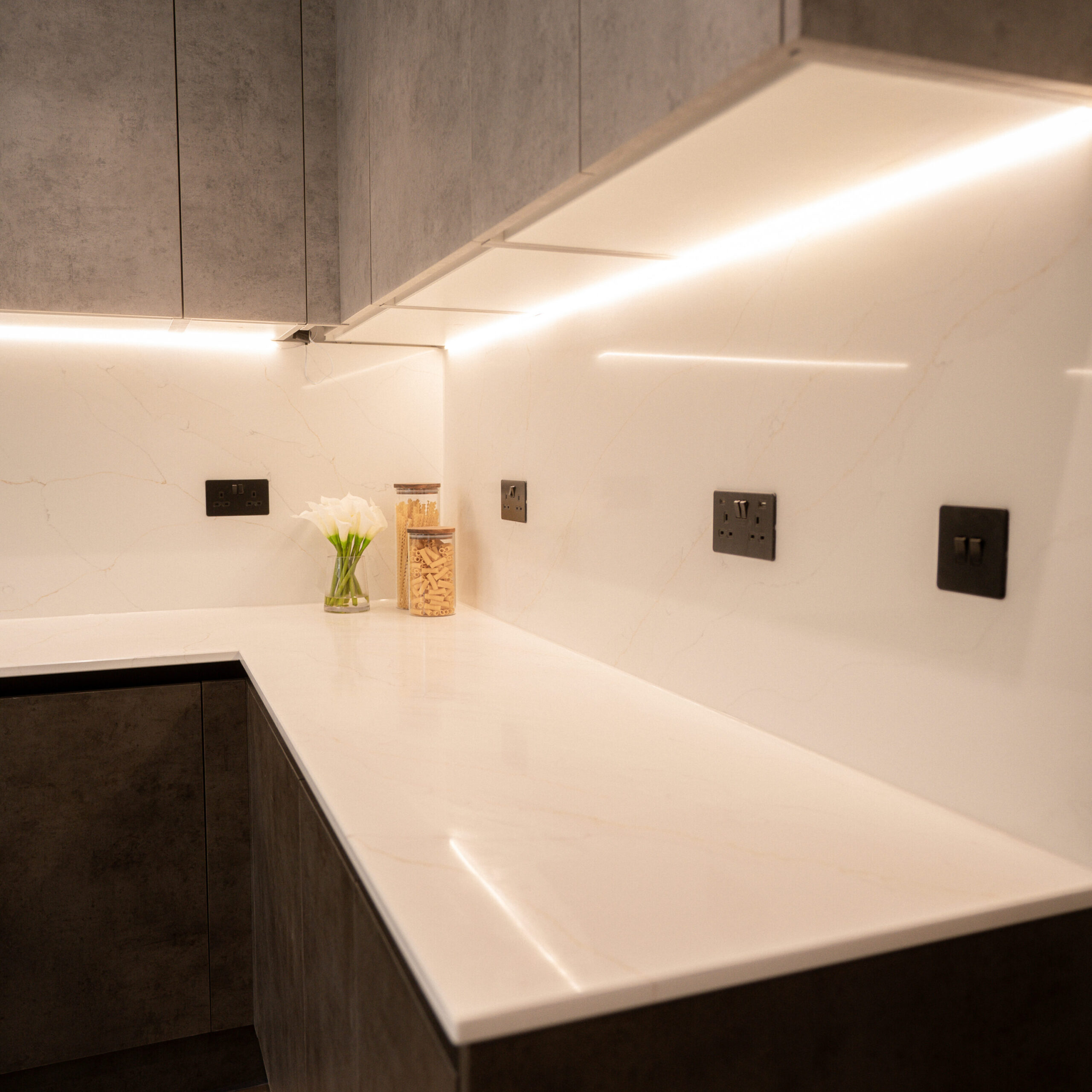 White marble tiling worktop and cplashback. Led lights underneath top cabinets. Slate/dark grey cabinets with slate grey power outlets
